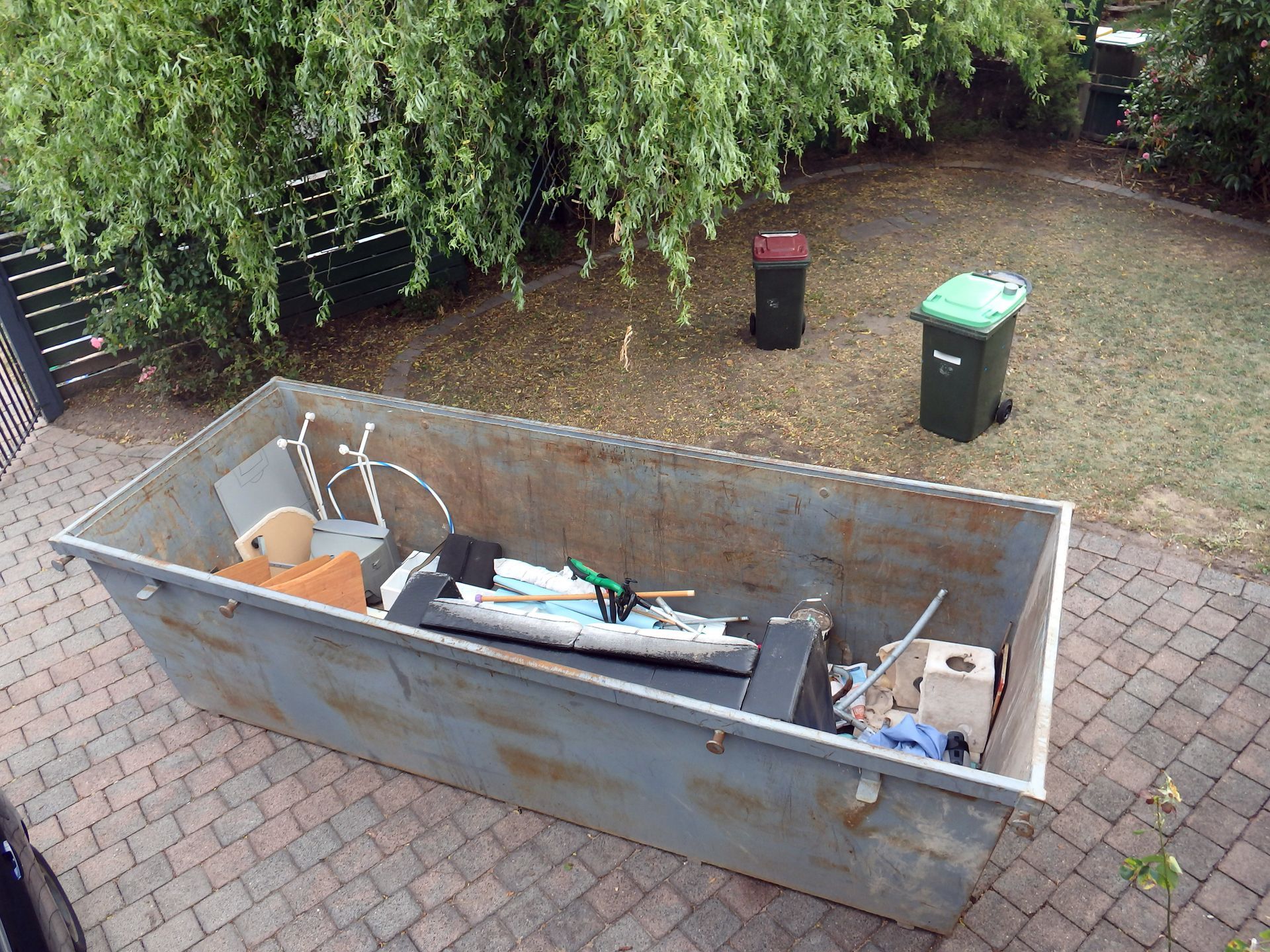 A dumpster filled with junk is sitting on a brick sidewalk.