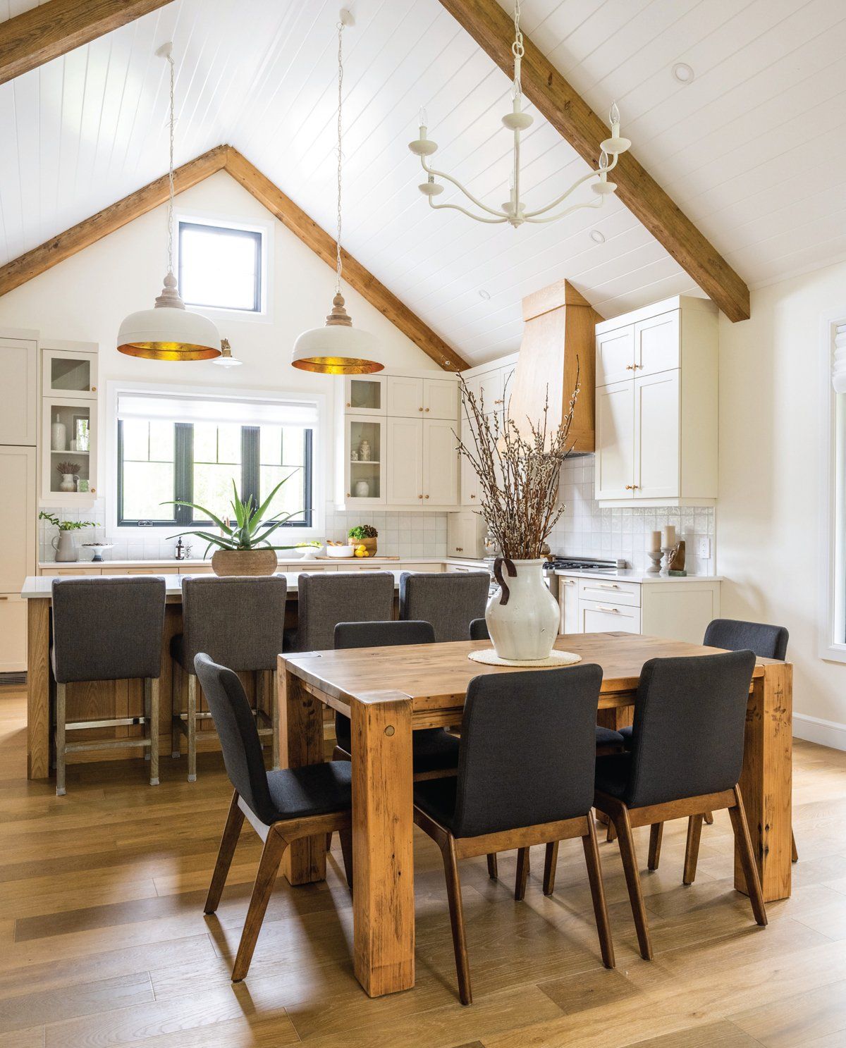 Rustic kitchen with wood beams, island seating, dining table, white cabinets, and hardwood floors.