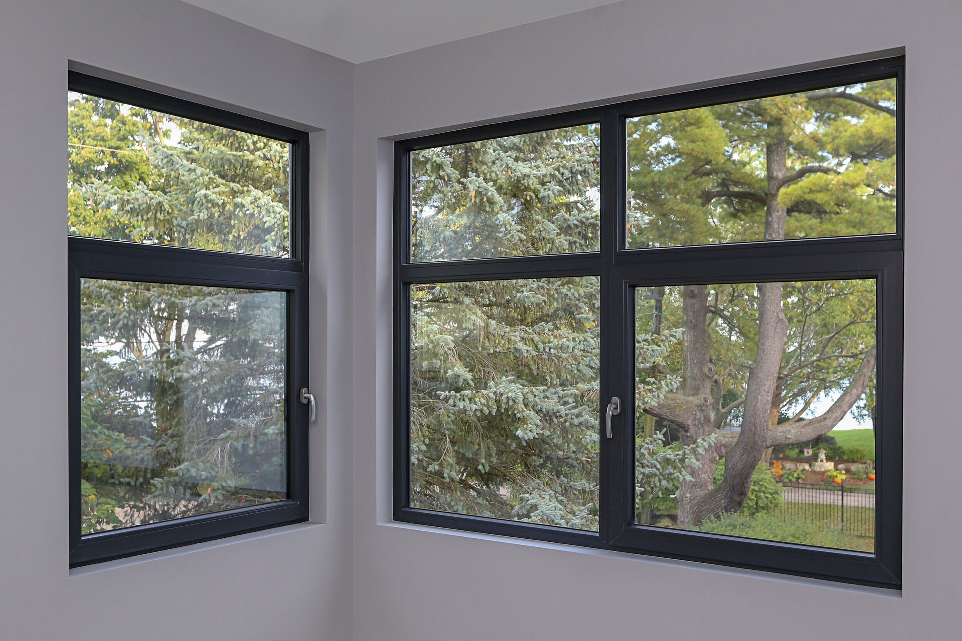 There are two windows in the corner of a room with trees in the background.