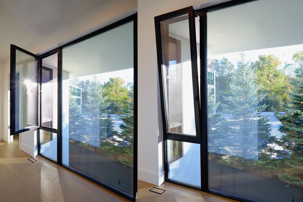Two views of a large window with black frames. One side is open, revealing trees outside. Sunlight streams in.
