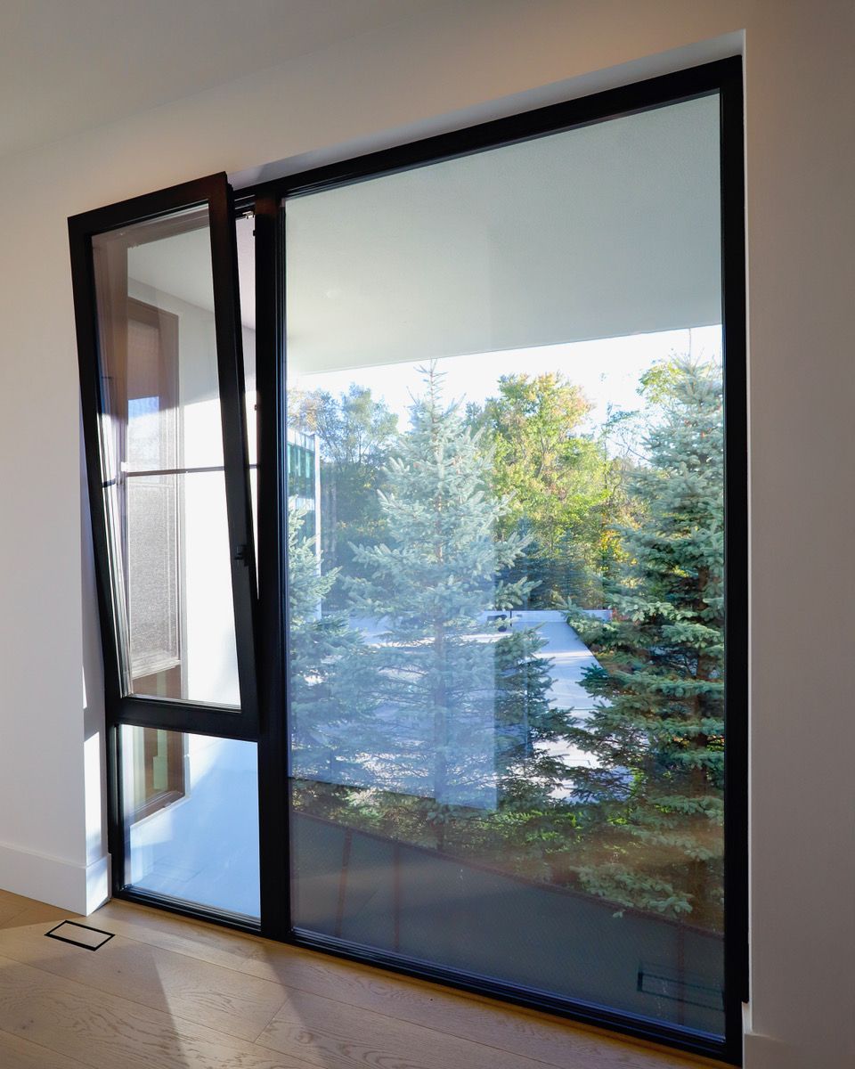 Black-framed window, one panel open, revealing a view of green trees and sky.