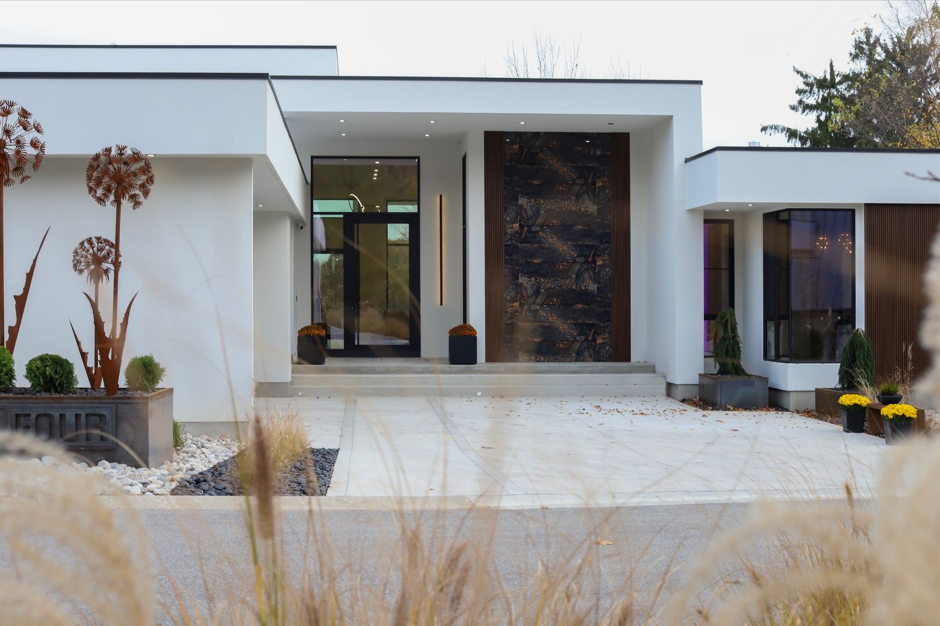Modern white house with large wooden door, glass entryway, and ornamental metal spheres.