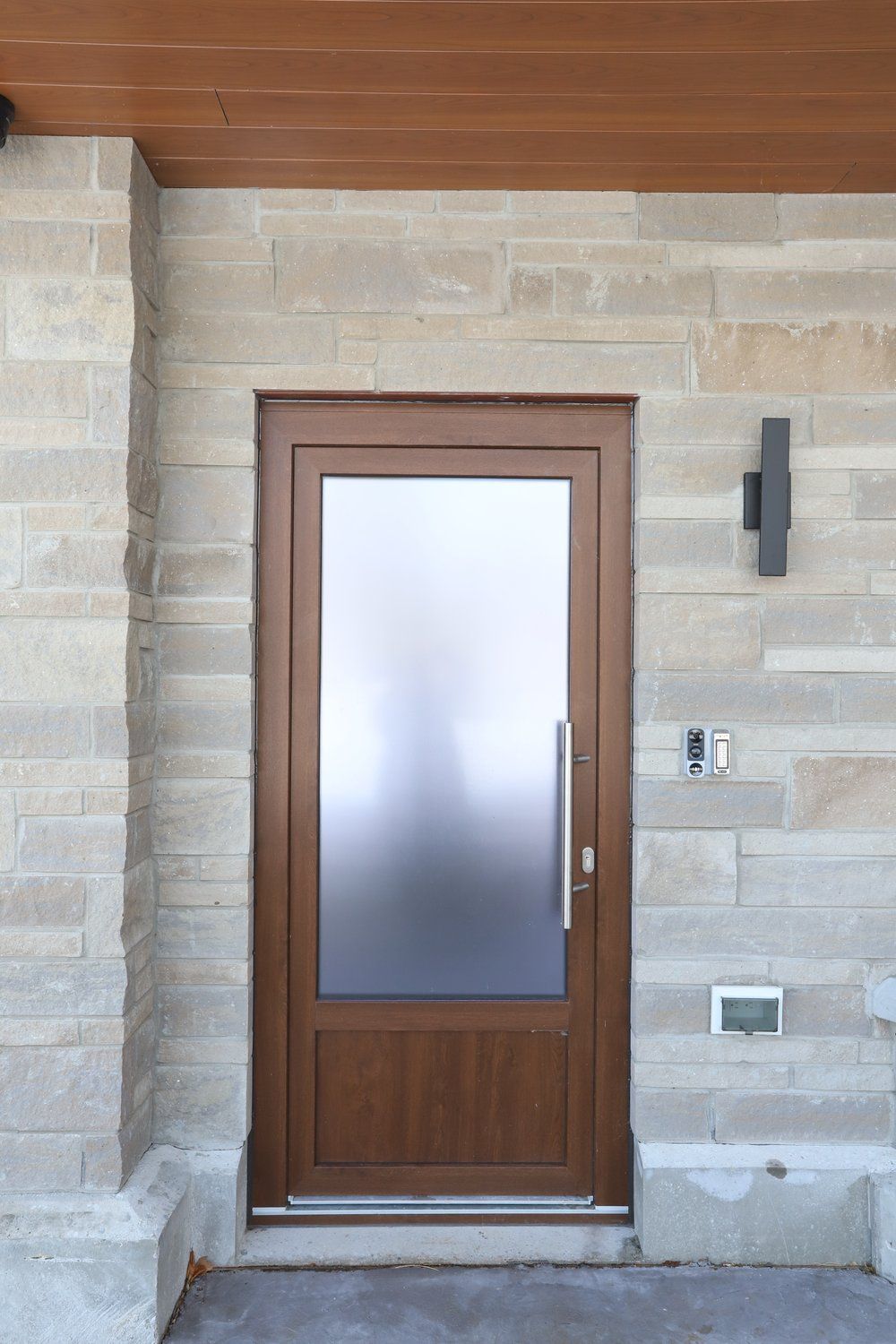 A wooden door with a glass window is on a brick wall.