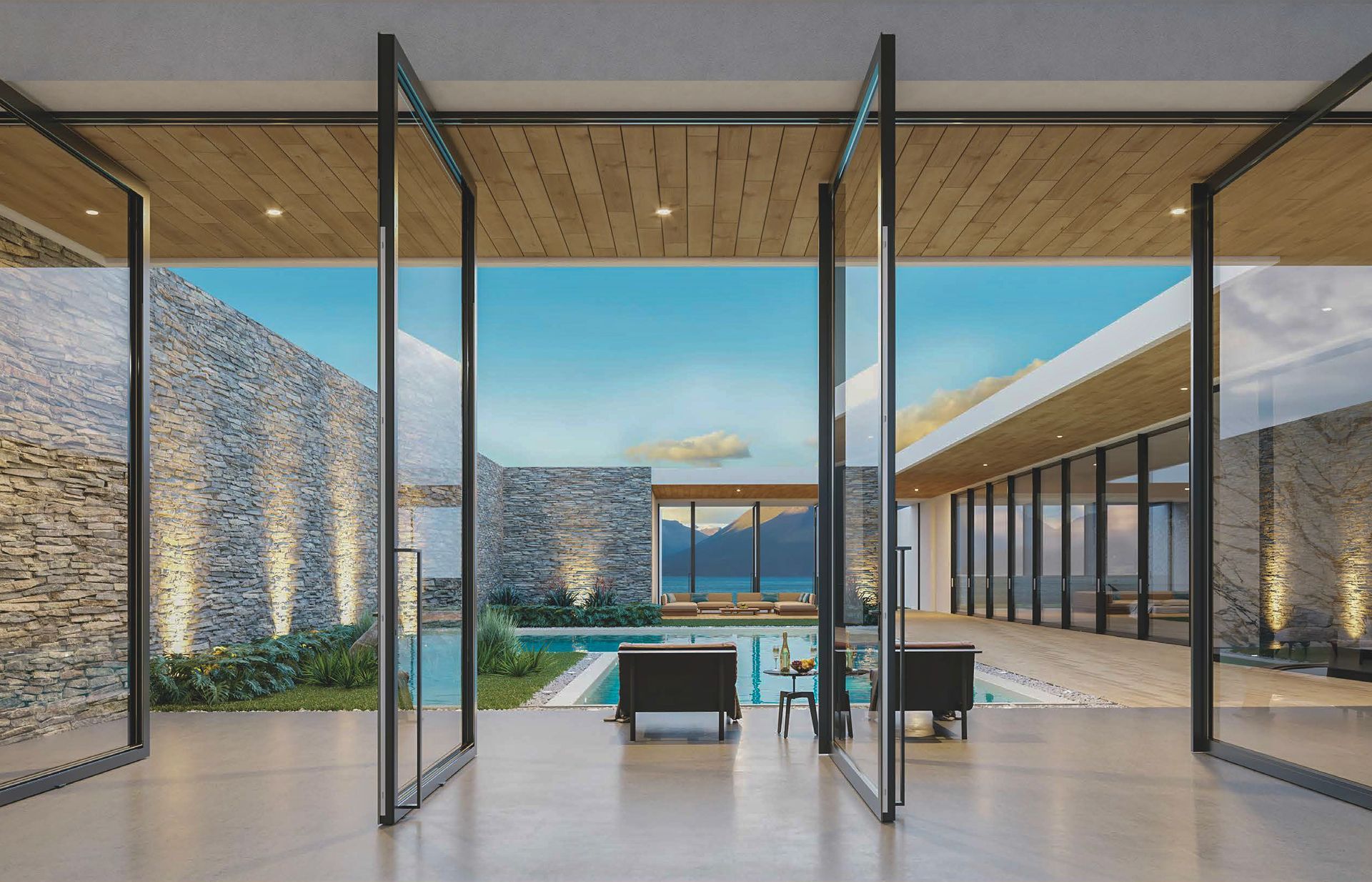 Large glass doors open to a pool and ocean view. Modern building with stone walls, lounge chairs, and blue sky.
