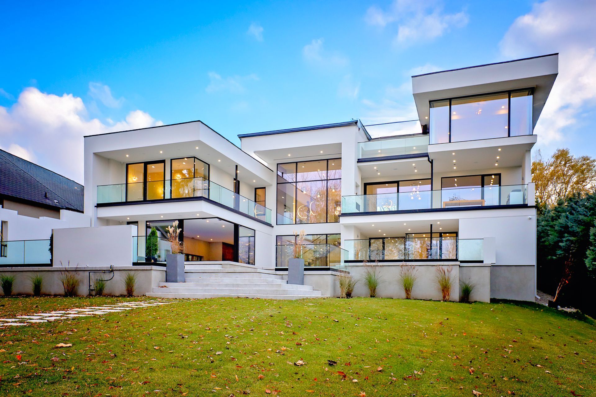 Modern white house with large windows and glass balconies against a blue sky.