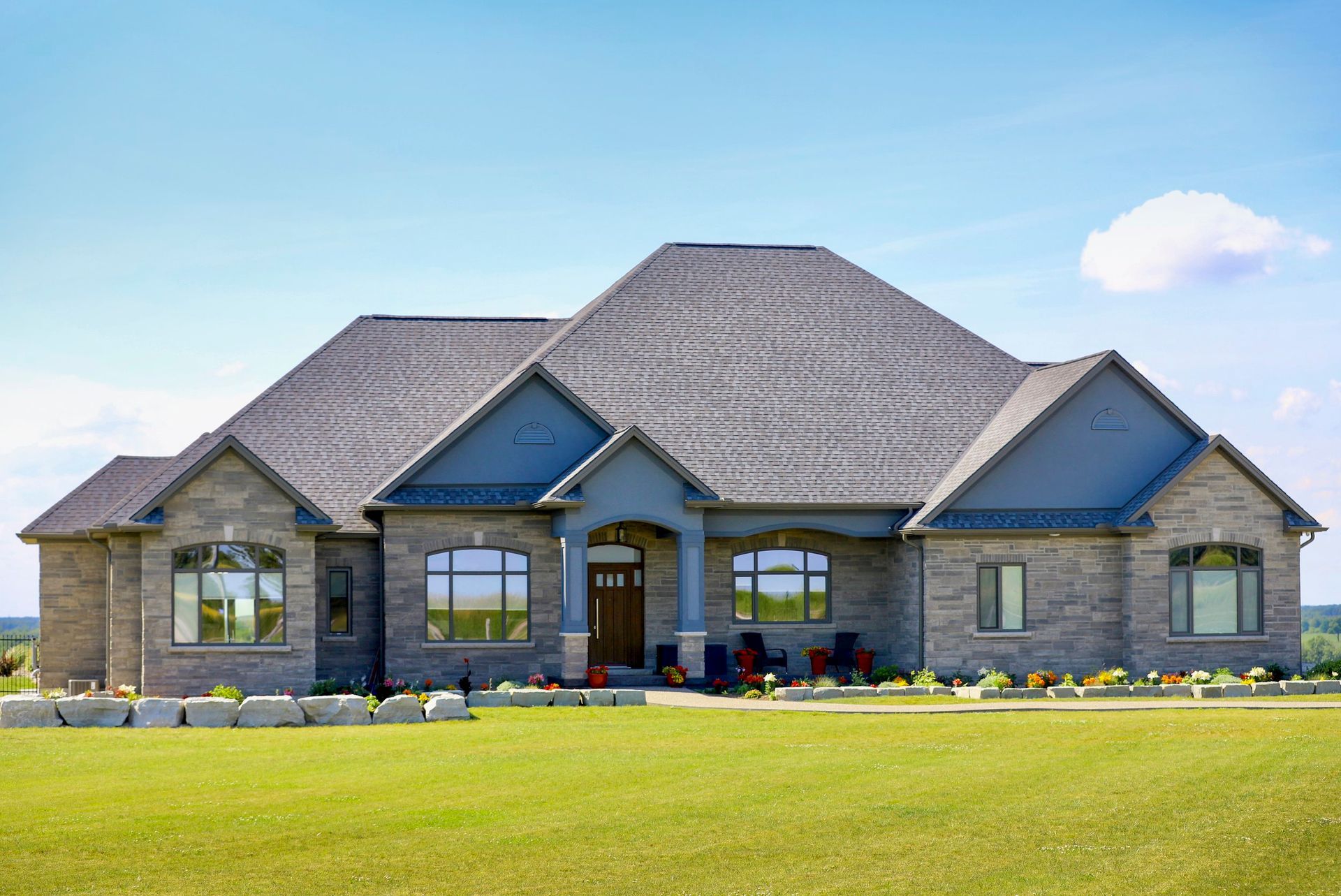 A large house with a gray roof is sitting on top of a lush green field.