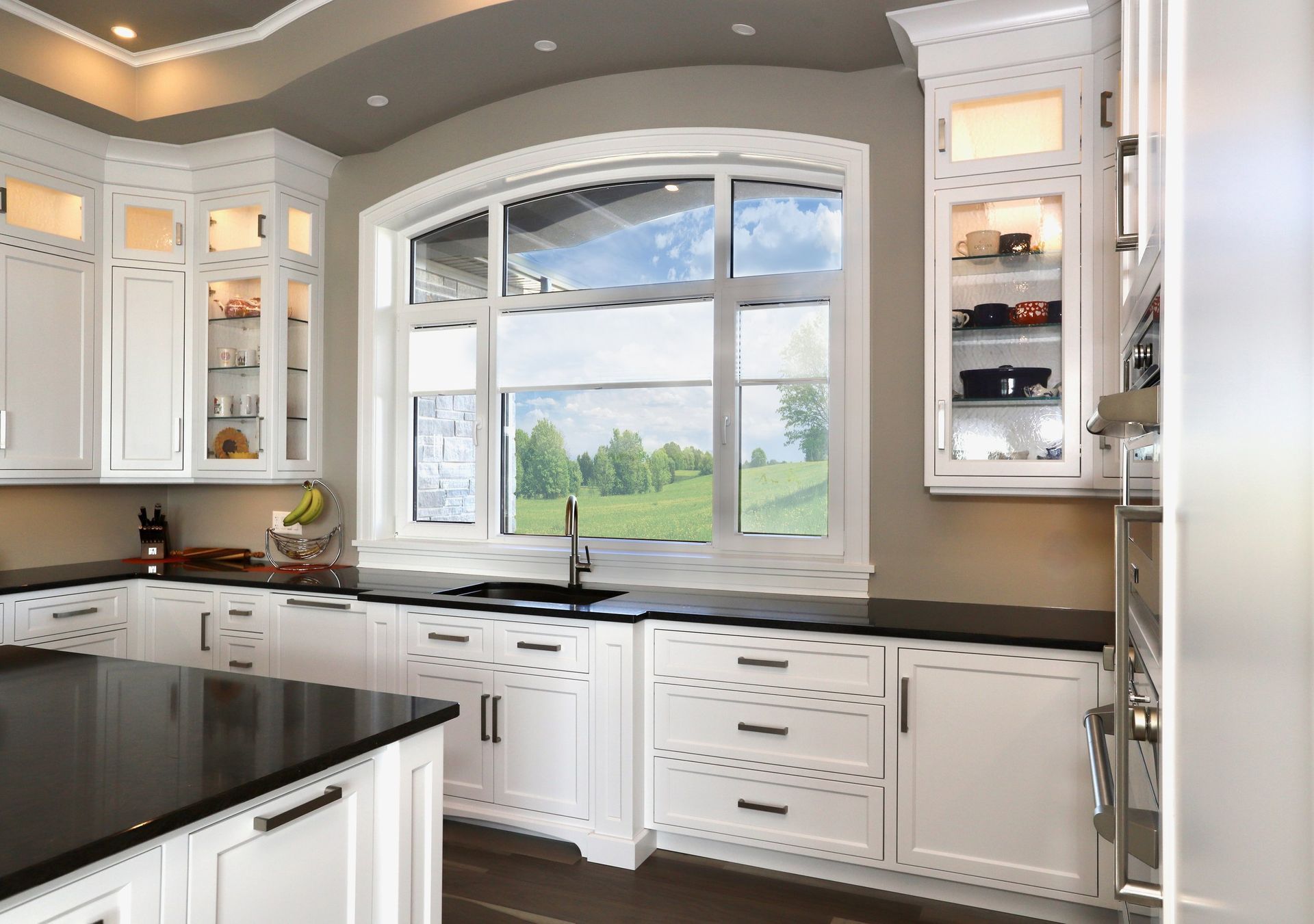 A kitchen with white cabinets and black counter tops and a large window.