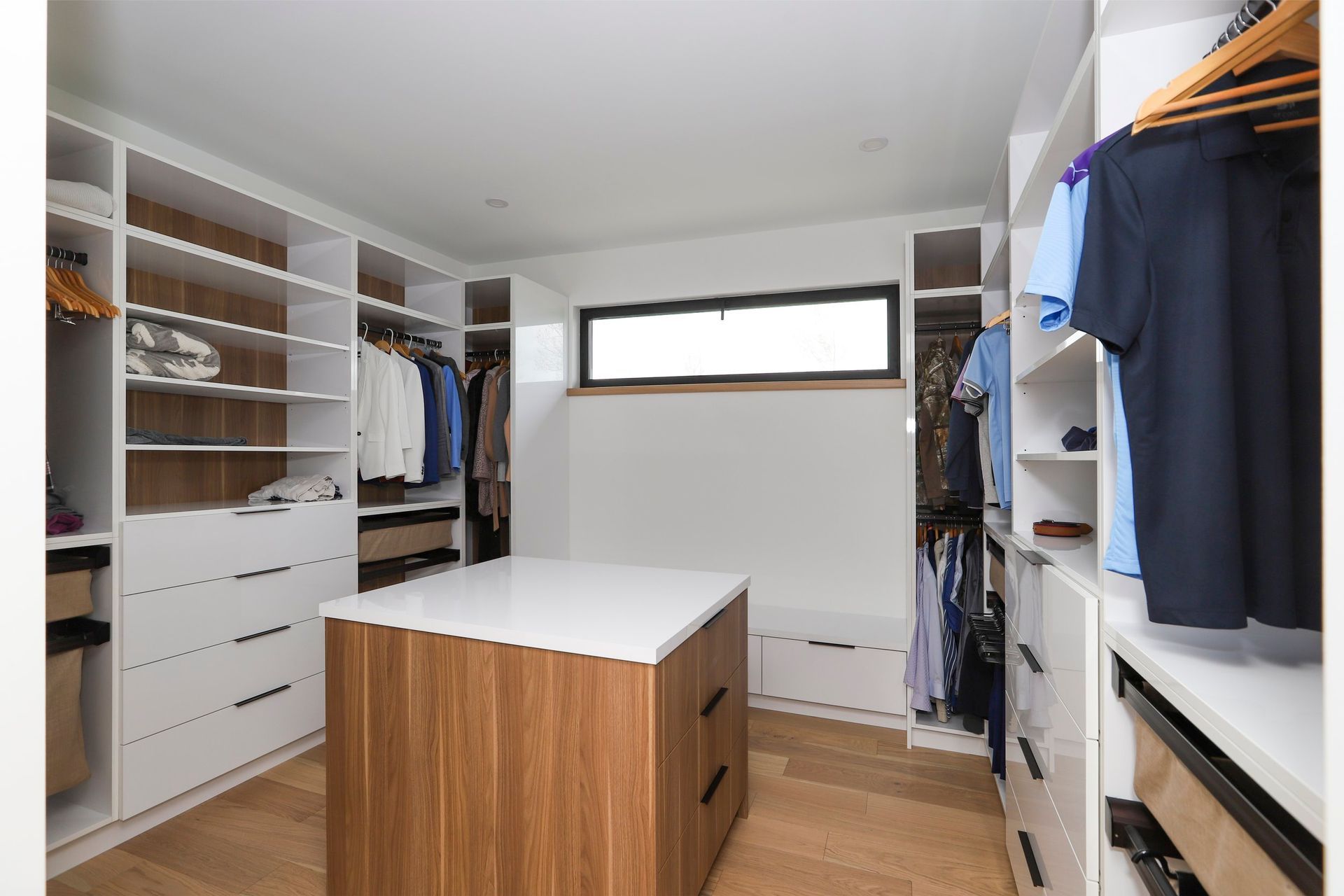 A walk in closet with lots of clothes and a large island in the middle.