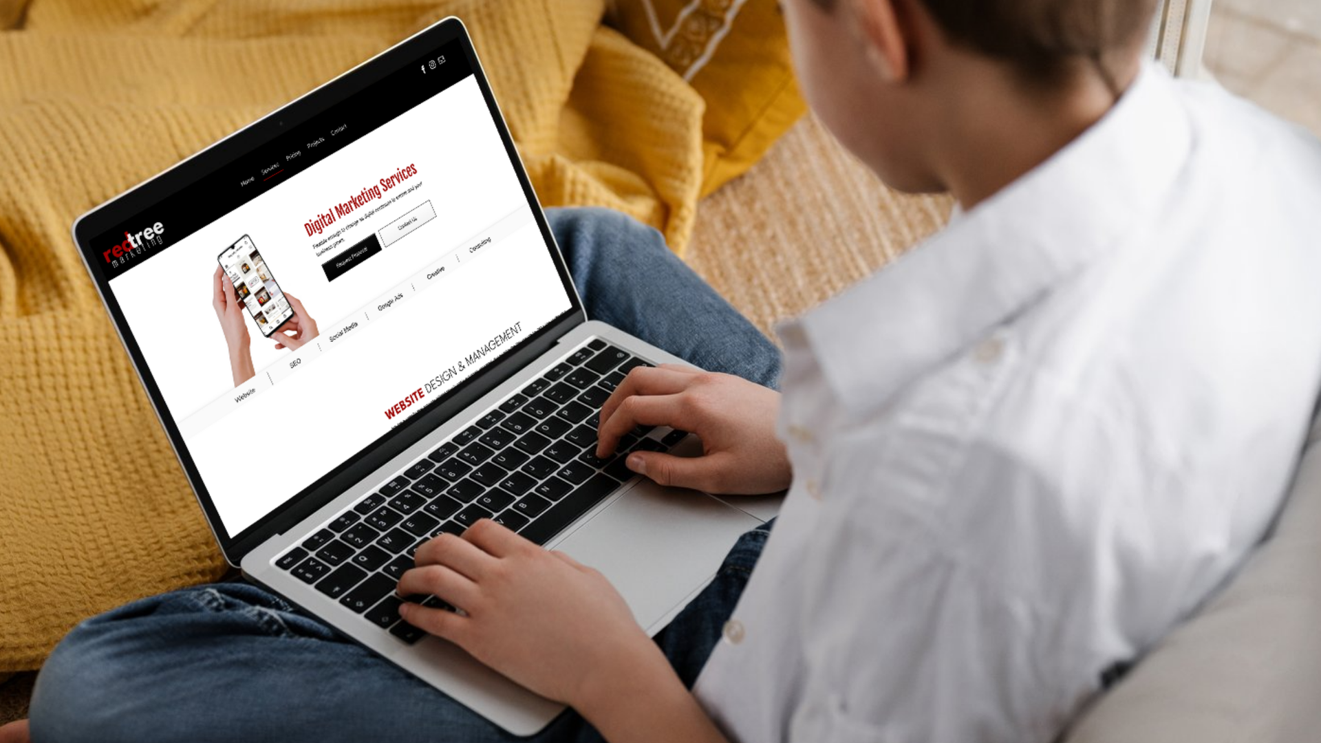 A young boy is sitting on a couch using a laptop computer.