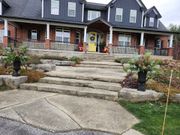 A rustic stone staircase leads up to the front entrance of a house with a dark metal roof and a bright yellow door.