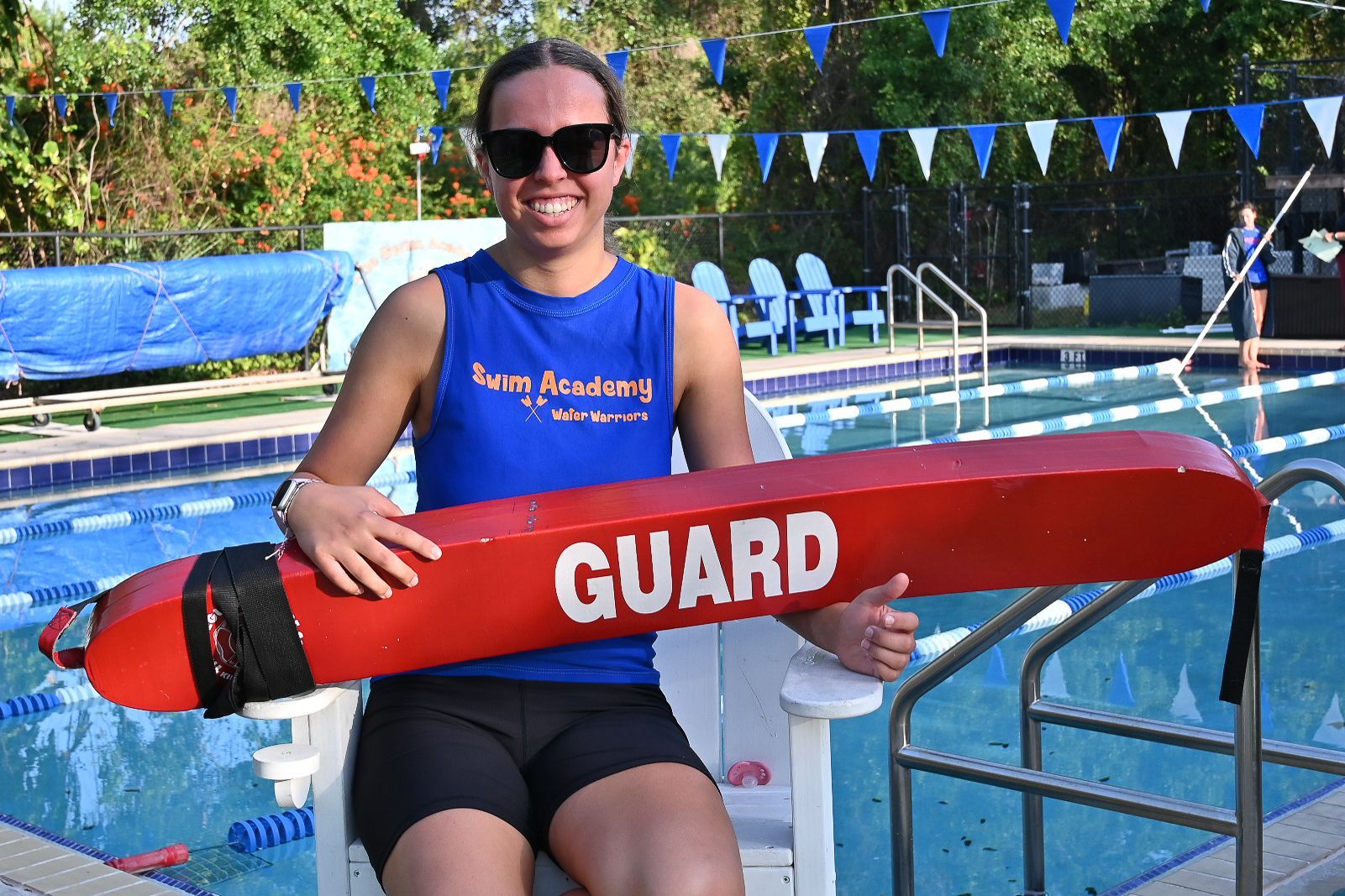 A woman is sitting in a lifeguard chair holding a red life preserver.