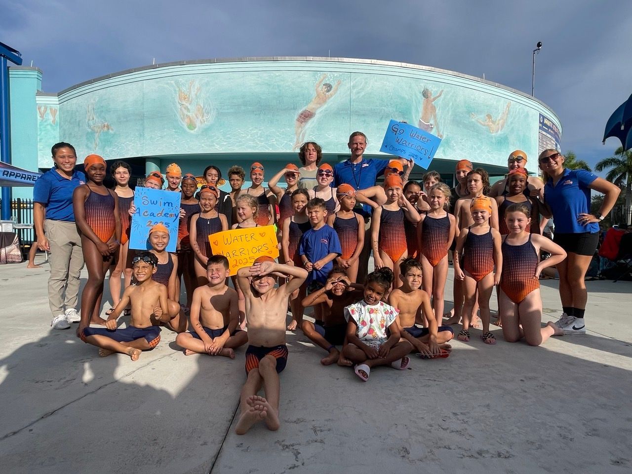 A group of children in swimsuits and swim caps are posing for a picture.