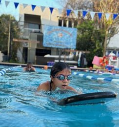A young girl is swimming in a pool with a surfboard.