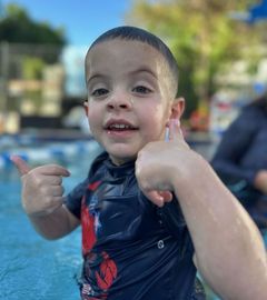 A young boy is giving a thumbs up in a swimming pool.