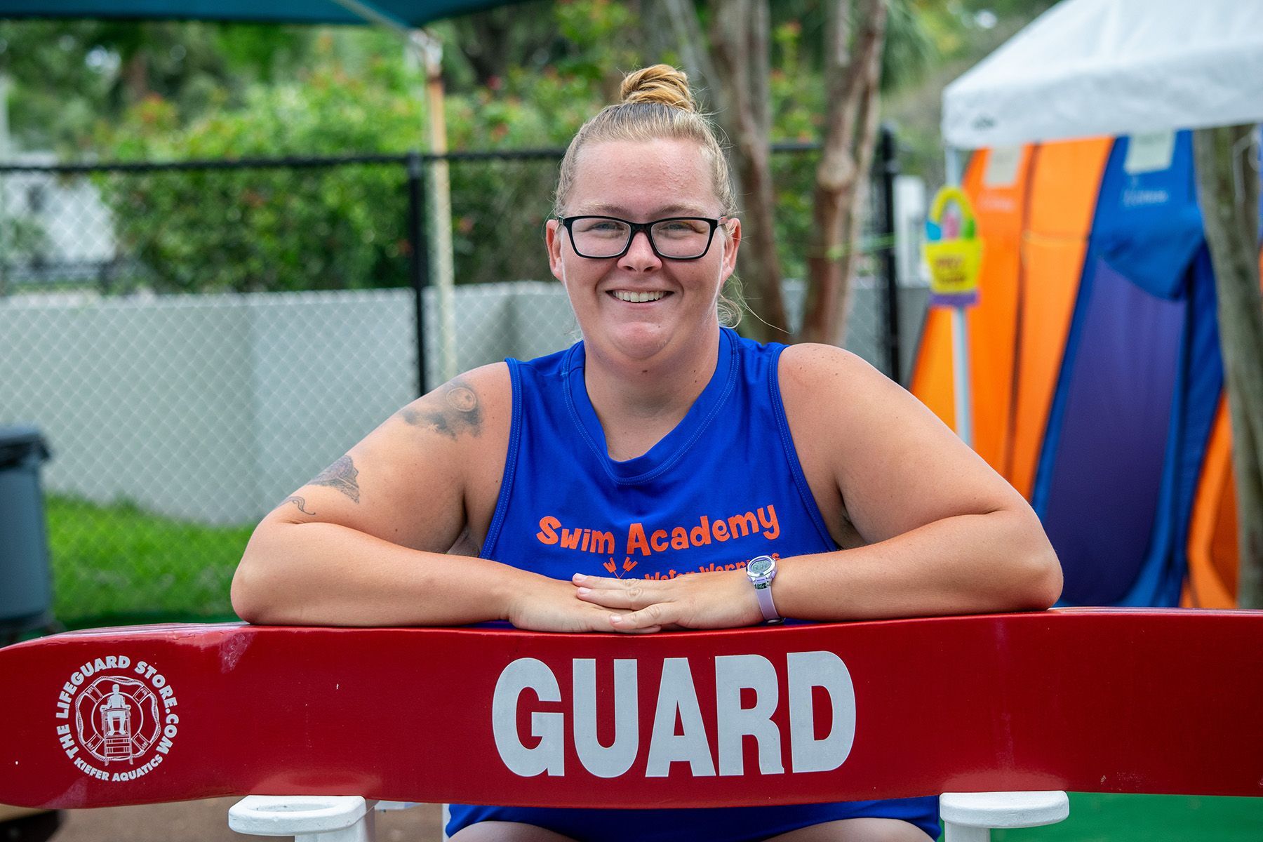 A woman in a blue tank top is sitting behind a red guard bar.