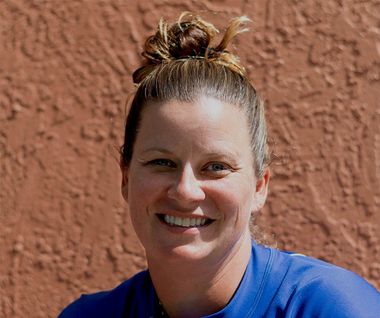 A woman in a blue shirt is smiling in front of a red wall.