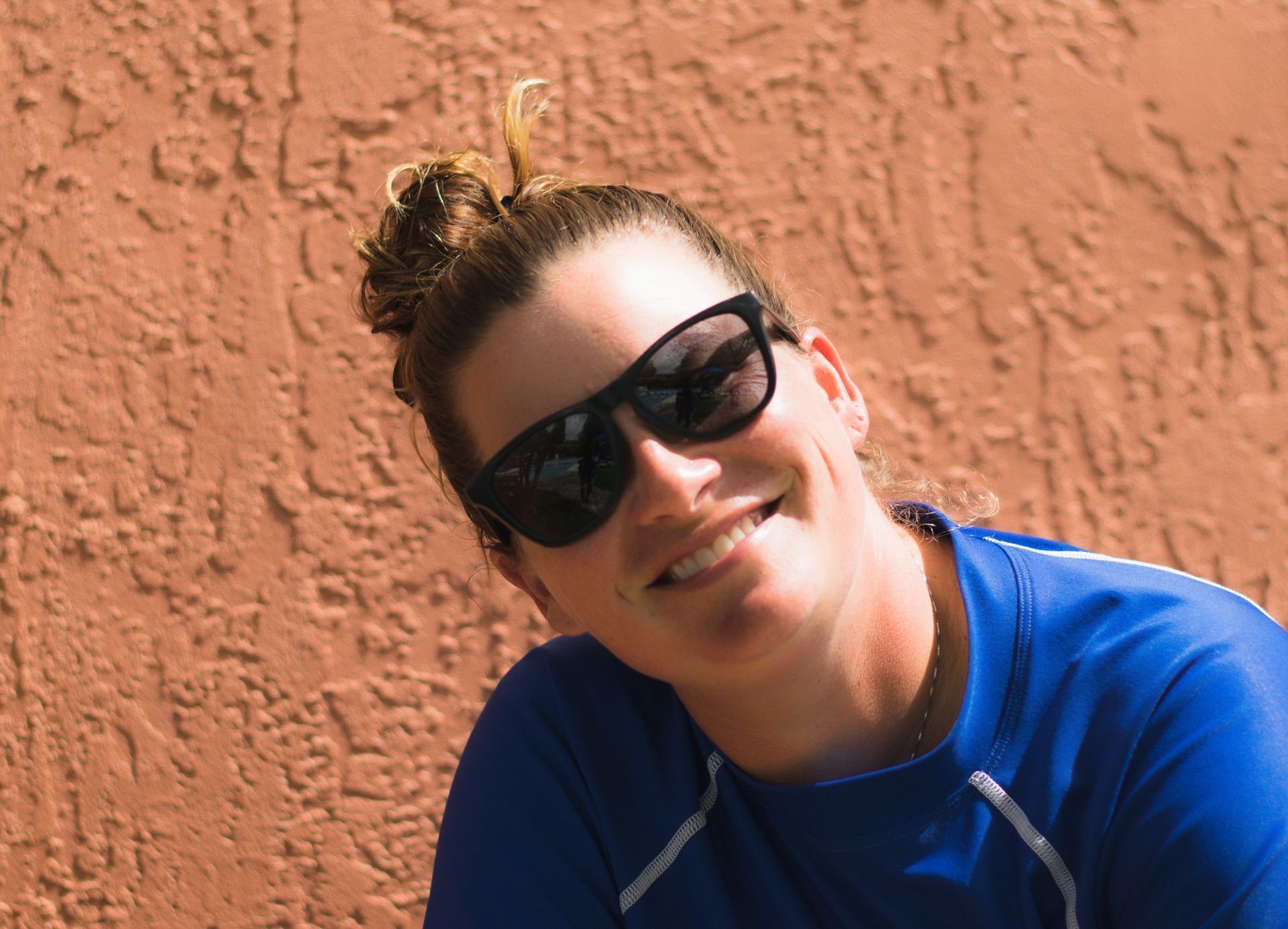 A woman wearing sunglasses and a blue shirt is smiling.