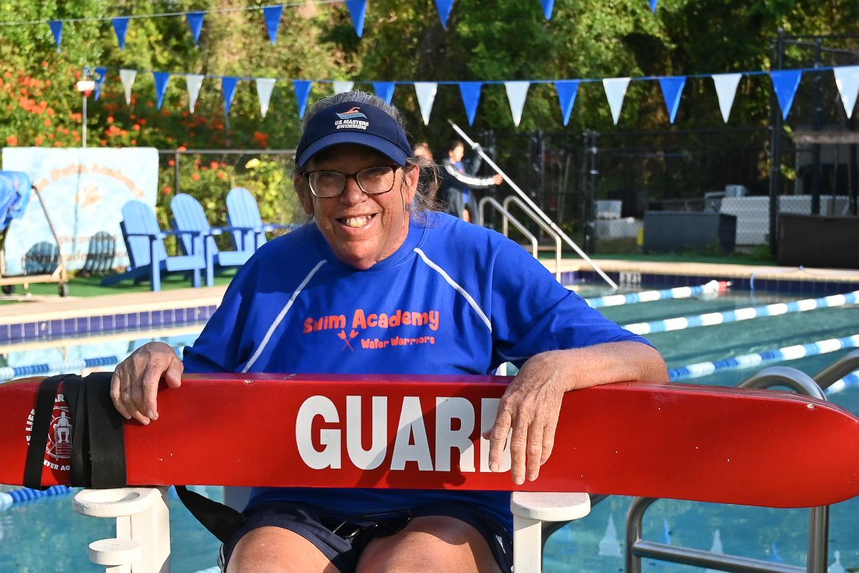 A man is sitting on a lifeguard chair holding a red life preserver.
