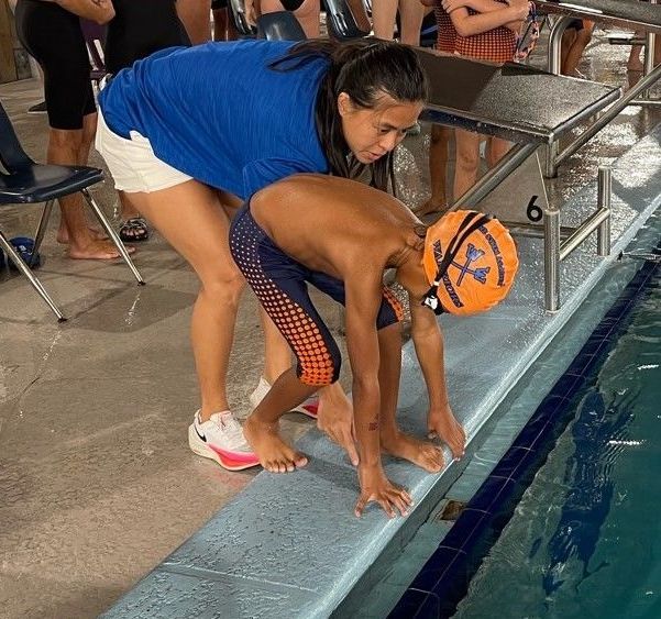 A woman helps a young boy get ready to swim in a pool