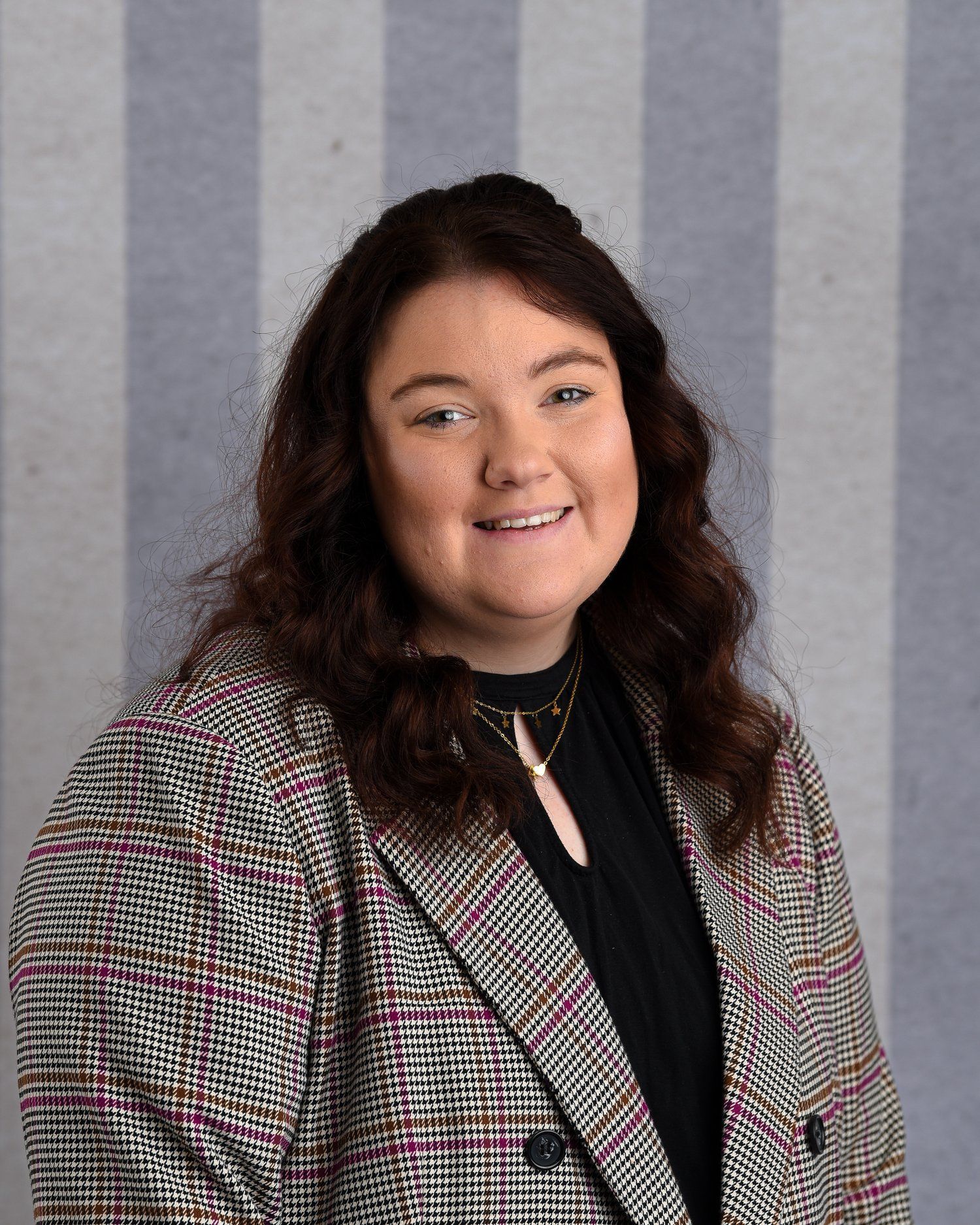 A woman wearing a plaid jacket and a black shirt is smiling for the camera.