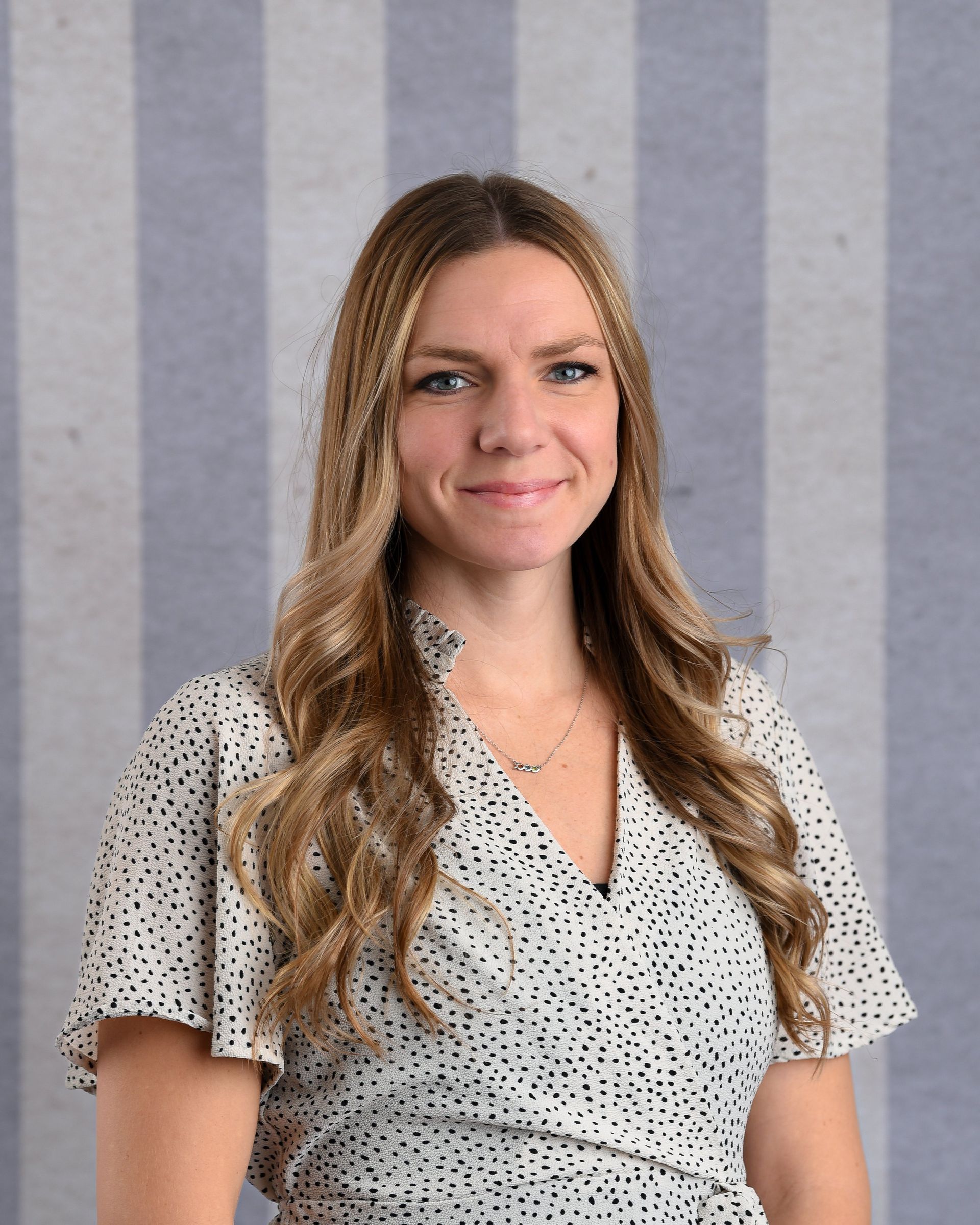 A woman in a polka dot dress is standing in front of a striped wall.