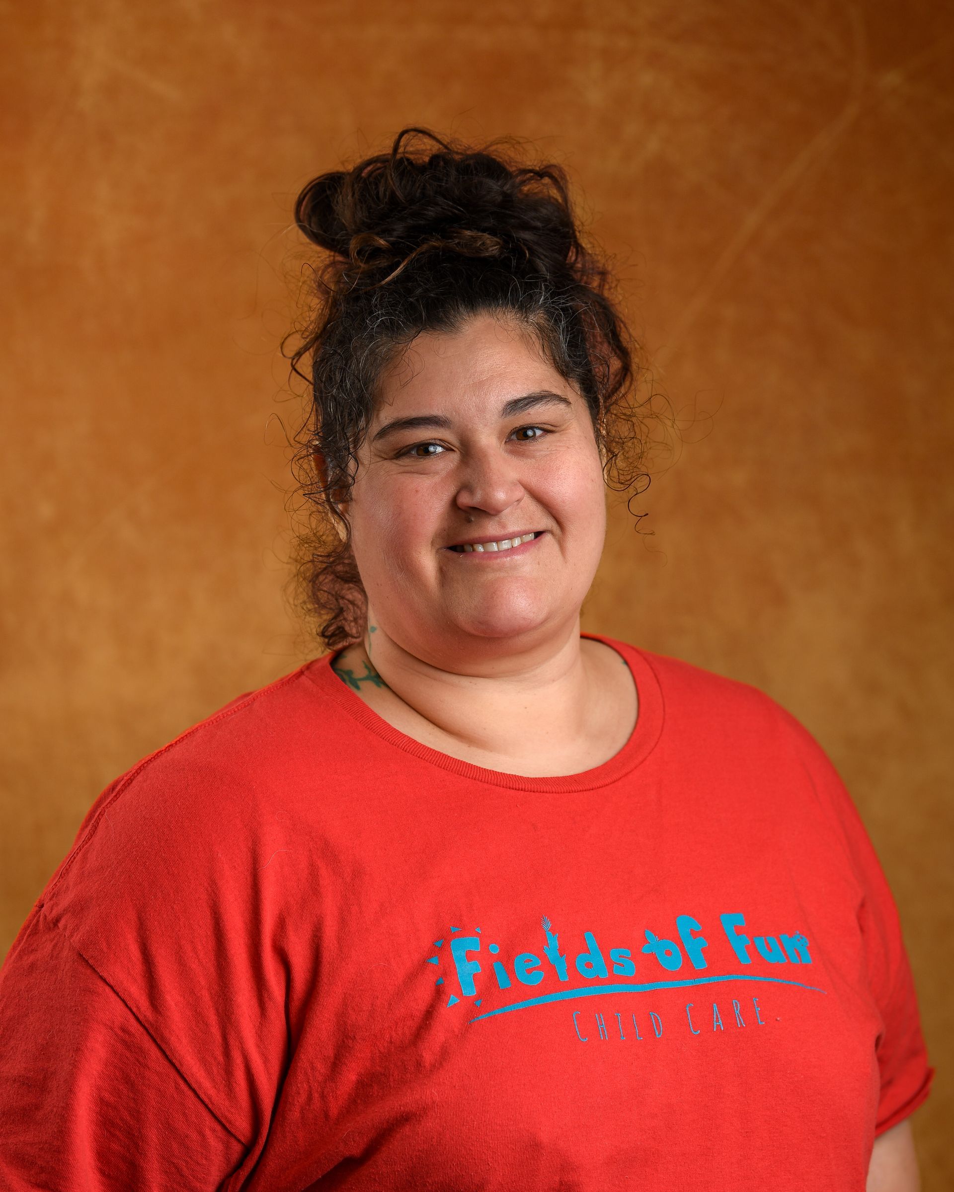 A woman wearing a fields of fun shirt is smiling for the camera.