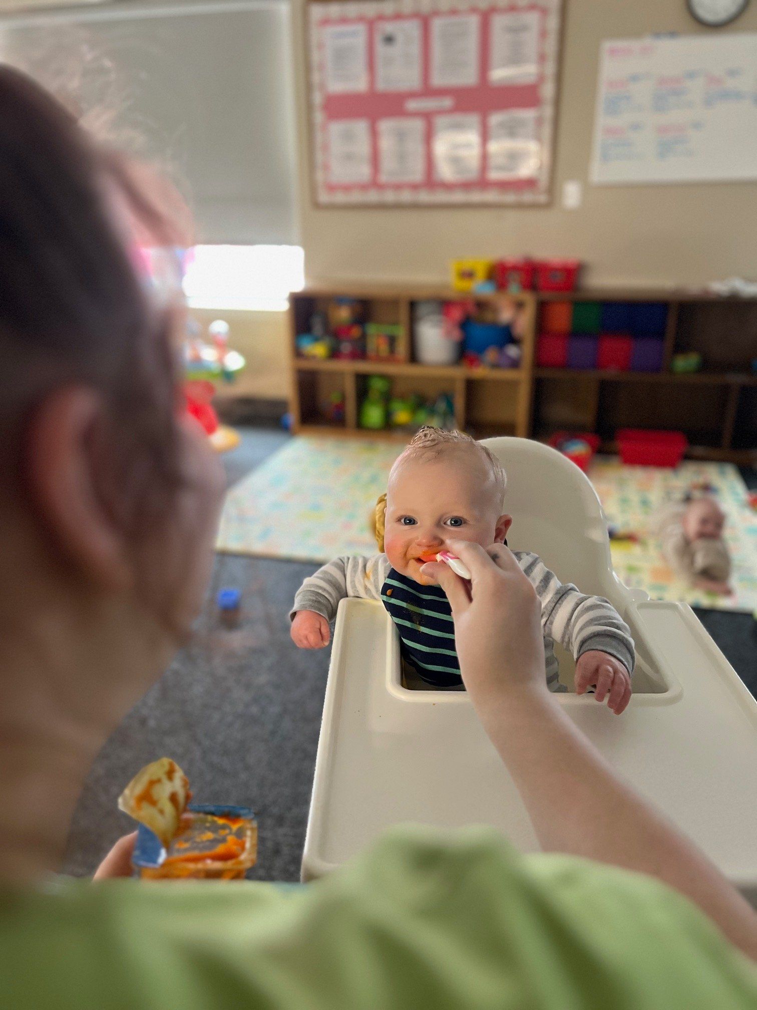 A woman is feeding a baby in a high chair.