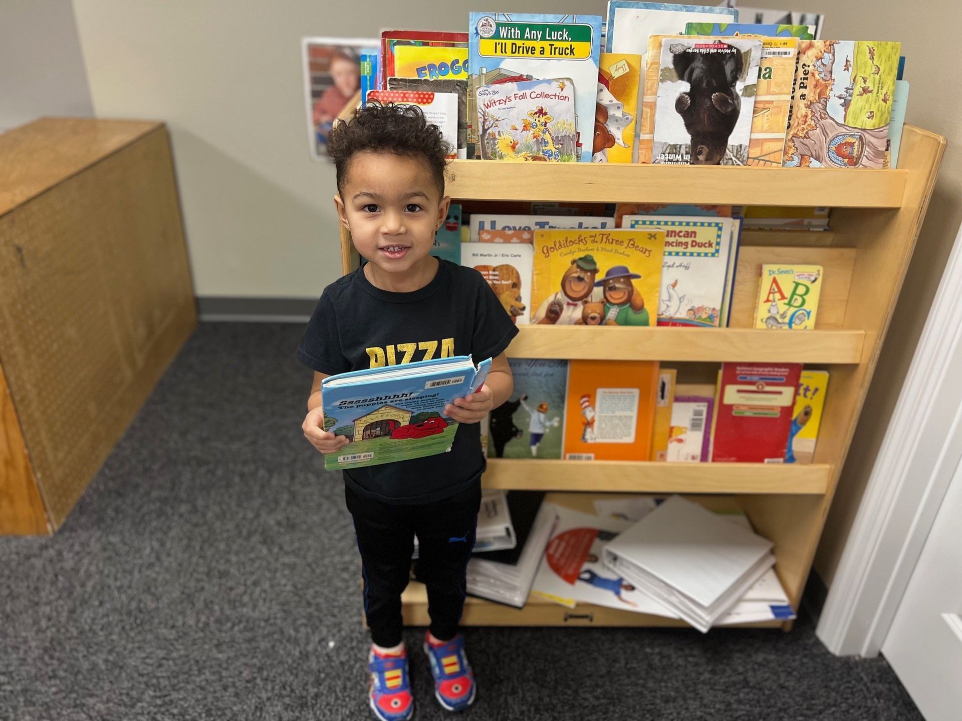 A young boy is holding a book in front of a bookshelf filled with books.