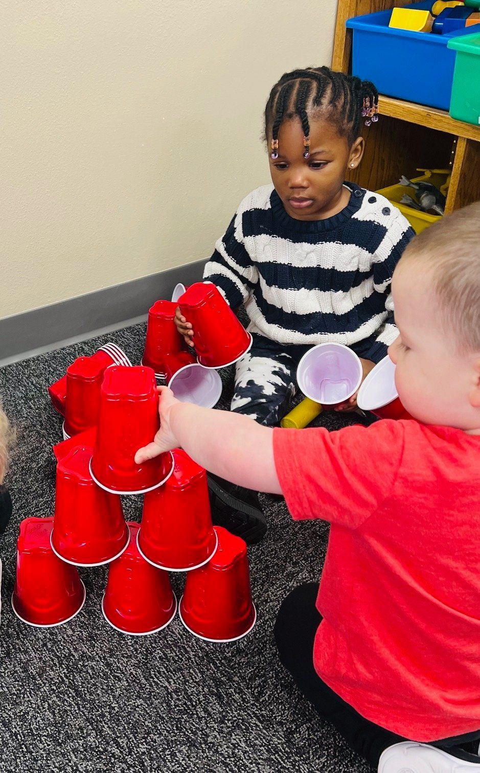 Two children are playing with red cups on the floor.