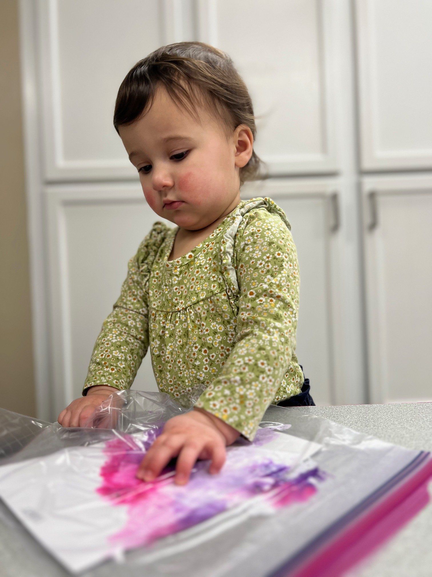 A baby is playing with pink and purple paint in a plastic bag.