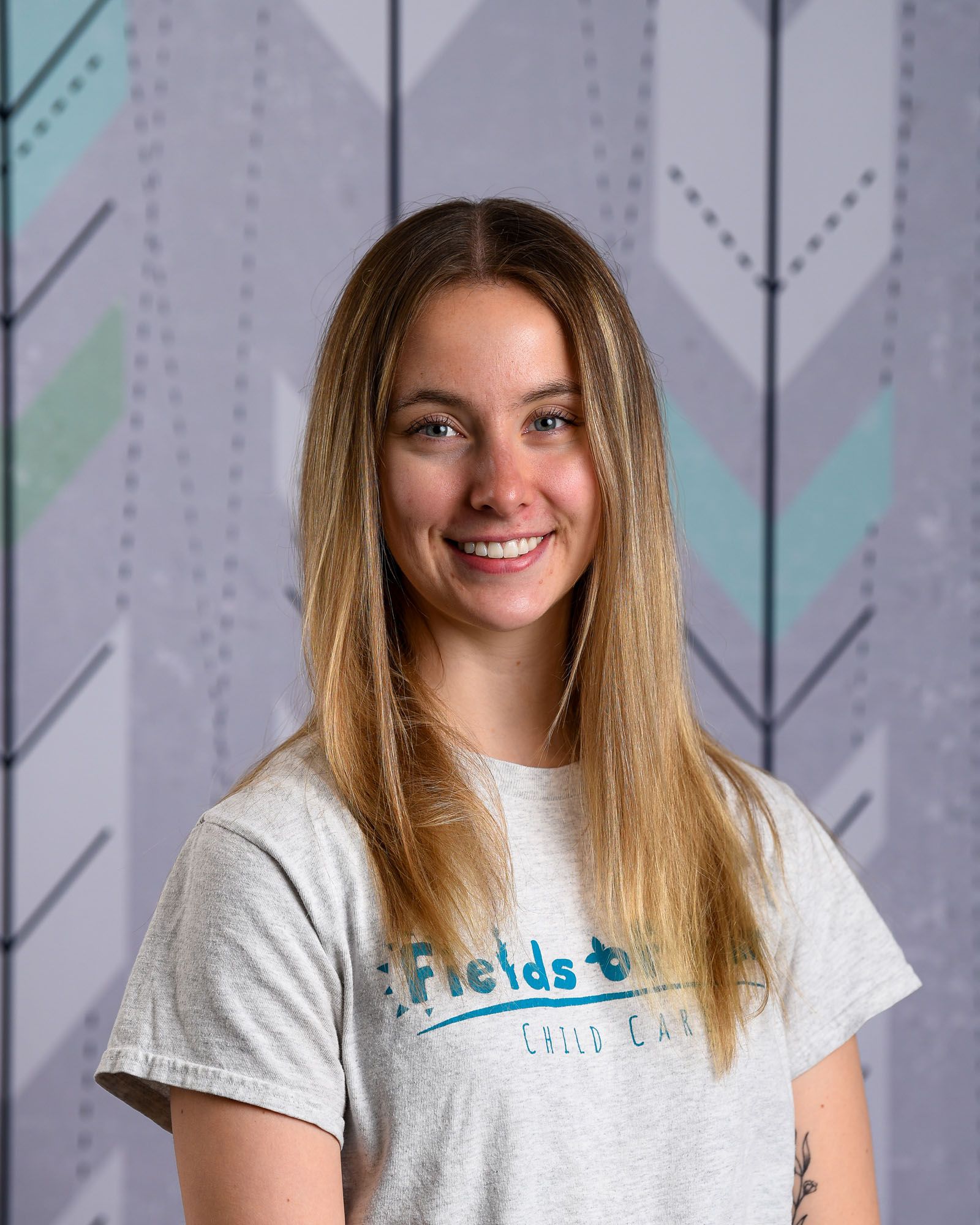A young woman wearing a gray sweatshirt is smiling in front of a striped wall.