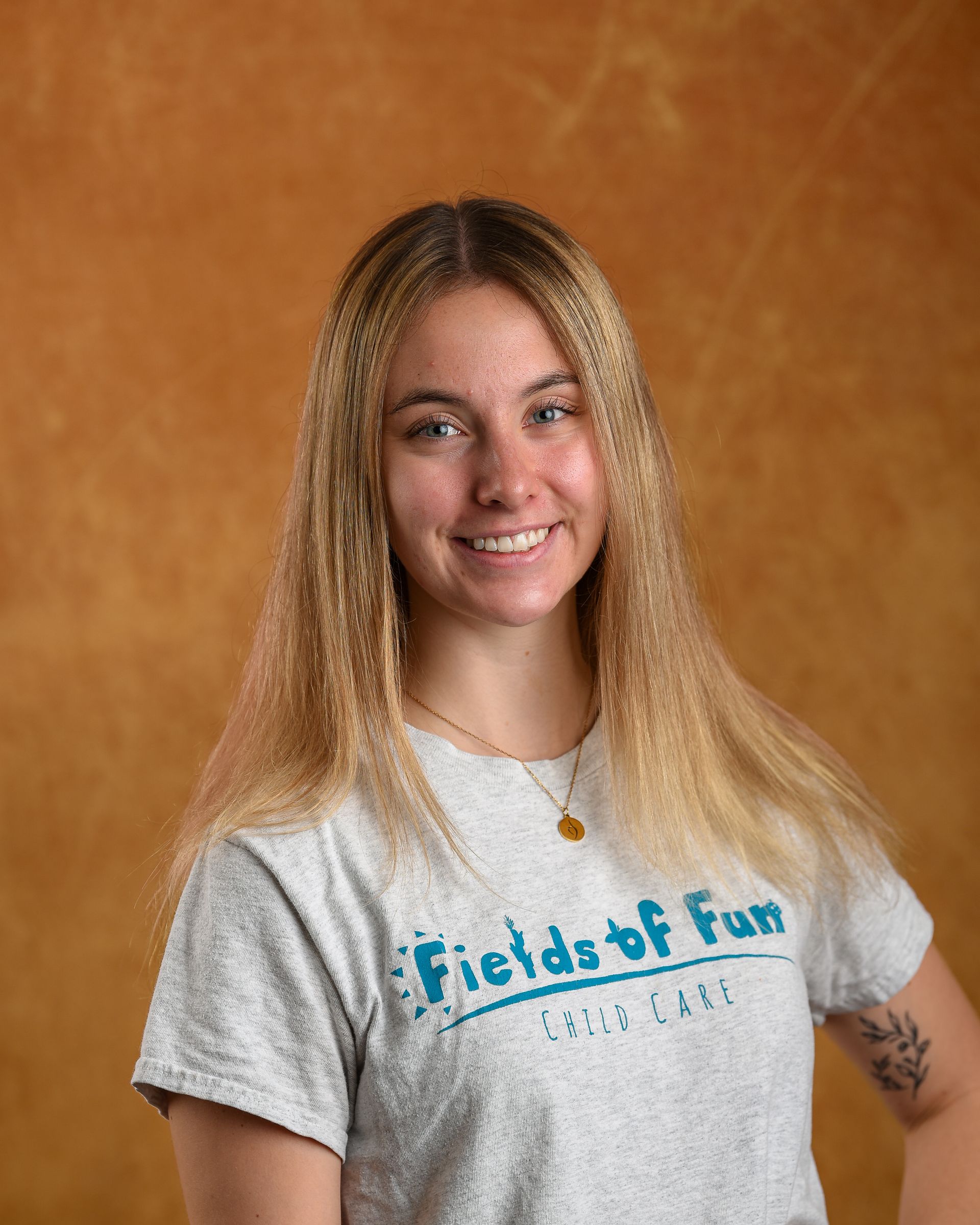 A young woman wearing a gray sweatshirt is smiling in front of a striped wall.