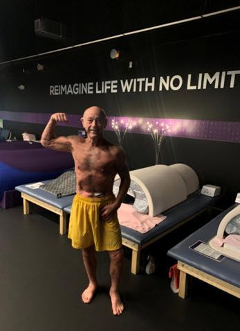 A man is flexing his muscles in front of a sign that says reimagine life with no limit