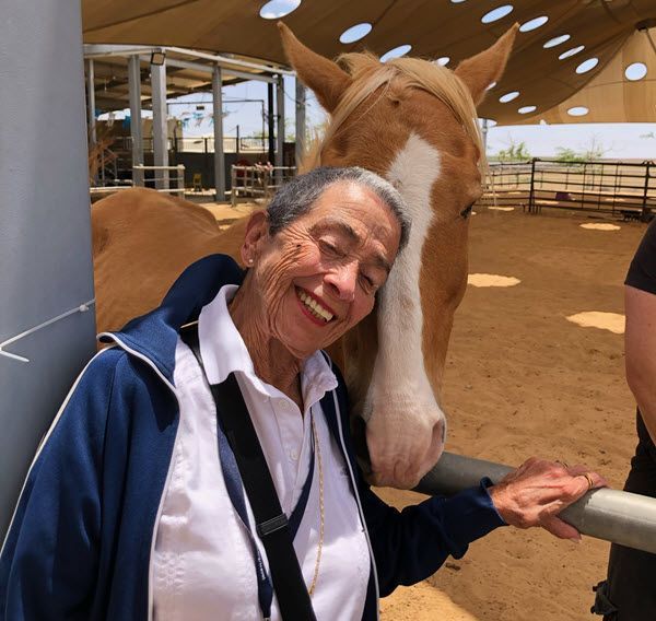 A woman in a blue jacket is petting a brown horse