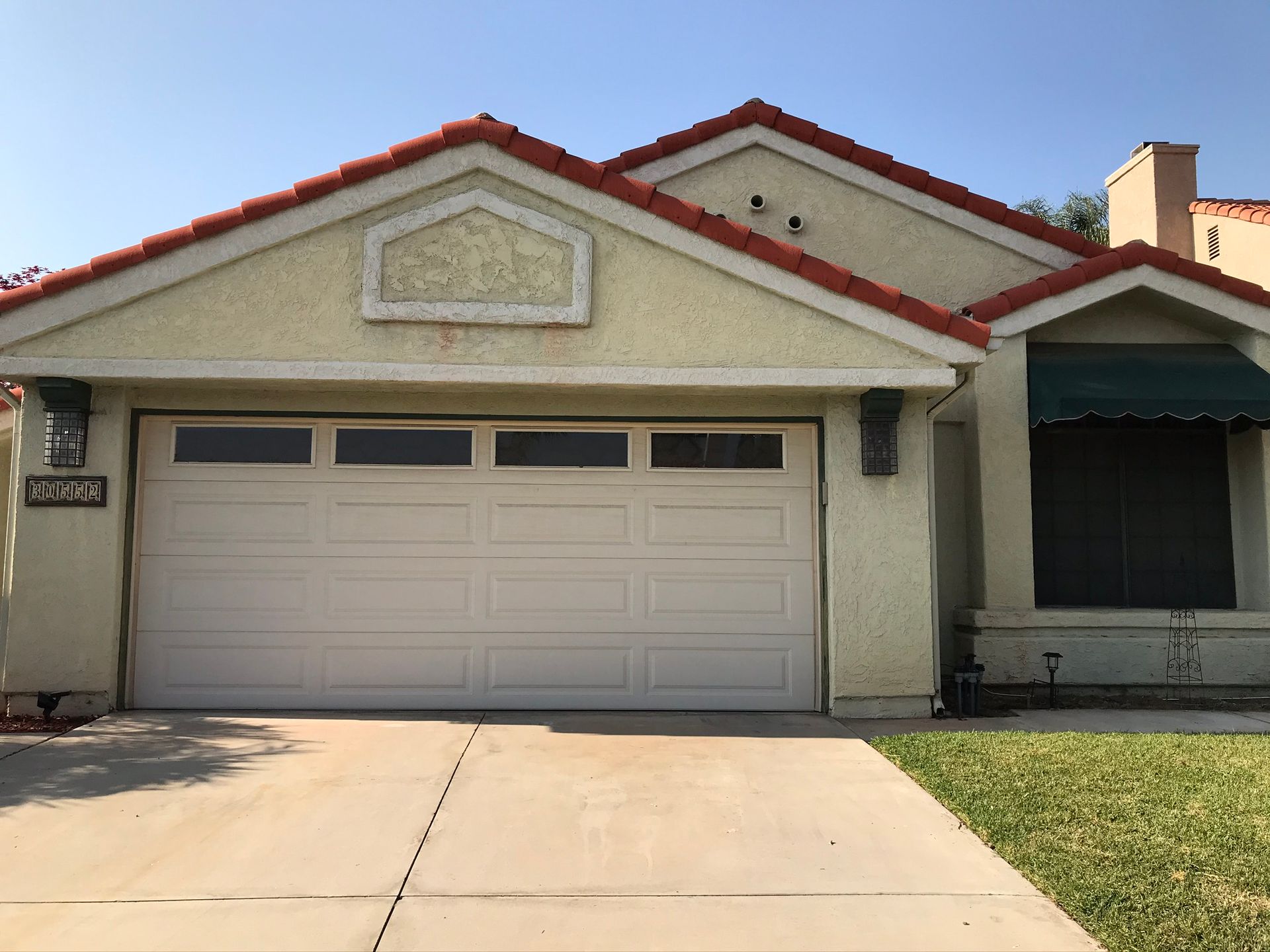 Single-story house with beige stucco, red roof trim, and a white double garage door