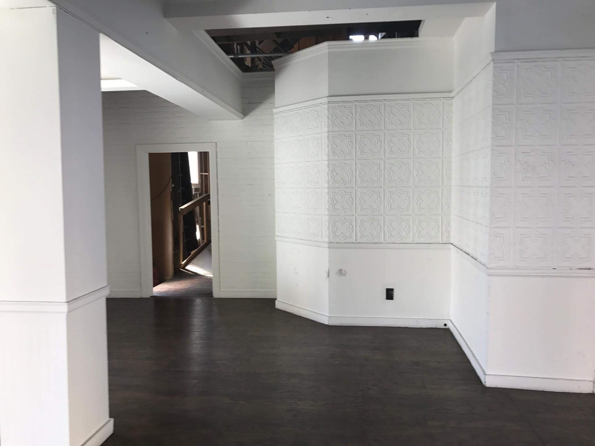 Empty white room with dark wood floors and built-in wall panels near a hallway opening