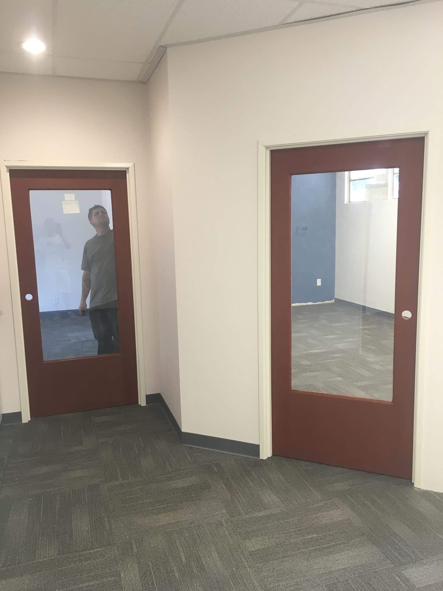 Hallway with two brown doors and carpeted floor; a person is visible through the left door window.