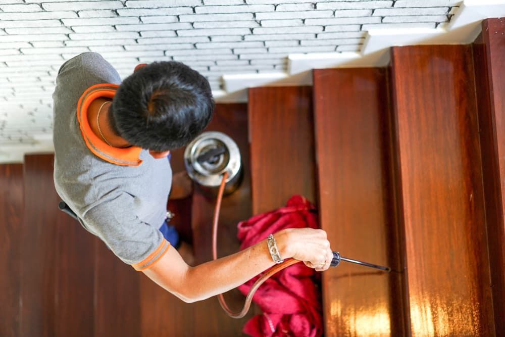 A Man Is Spraying Insecticide on A Wooden Staircase — Pest Control Central Coast in Woy Woy, NSW