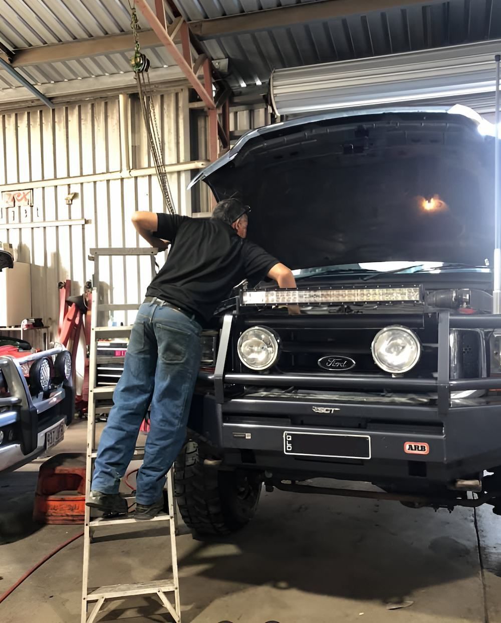 A Man Is Working On The Hood Of A Truck In A Garage — Mackay Car & Commercial Pty Ltd In Paget, QLD