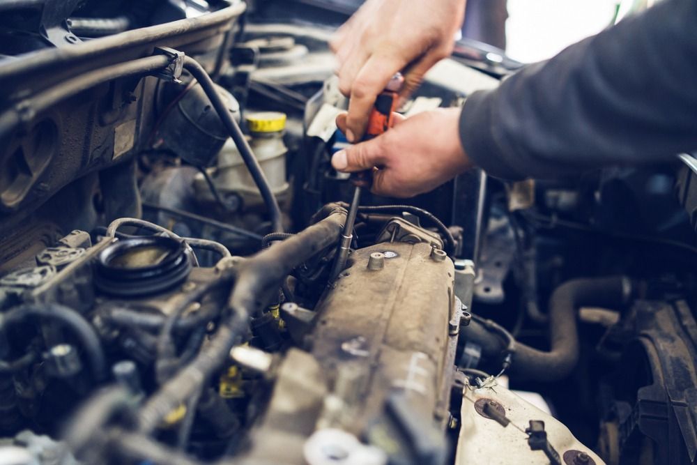 A Man Is Working On The Engine Of A Car With A Screwdriver — Mackay Car & Commercial Pty Ltd In Paget, QLD