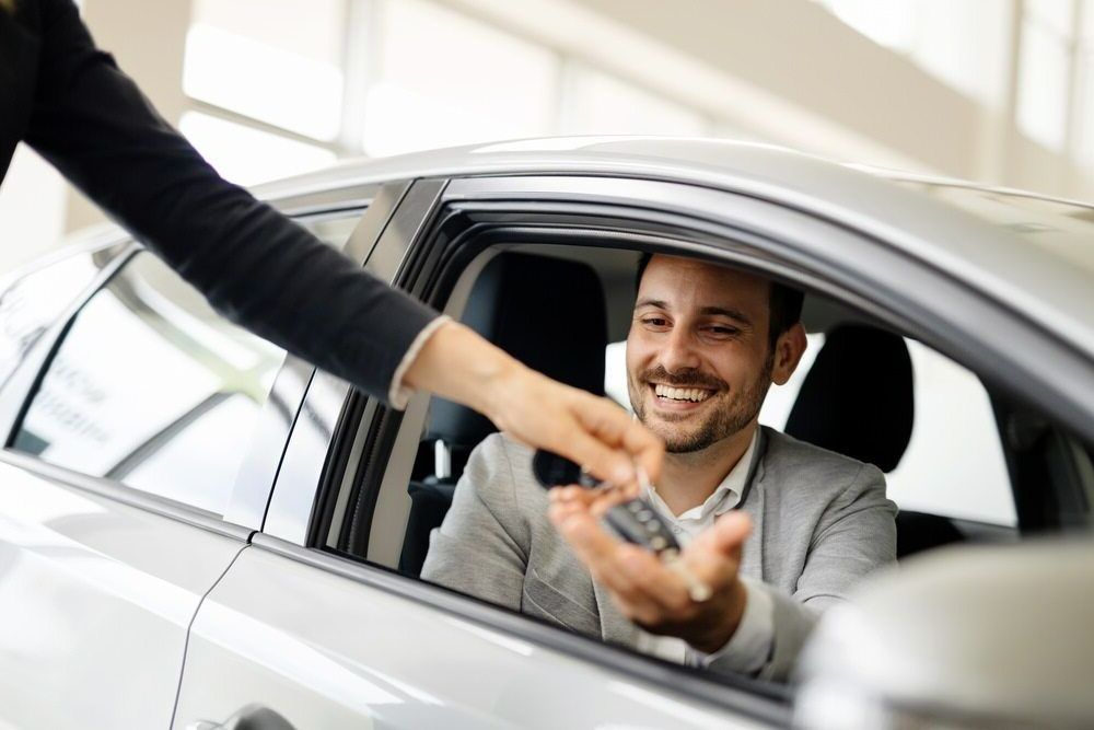 A Man Is Sitting In A Car Getting A Car Key From A Woman — Mackay Car & Commercial Pty Ltd In Paget, QLD