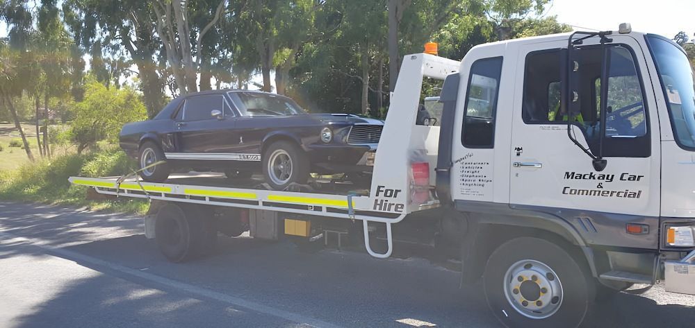 A Tow Truck Is Carrying A Black Car On The Back Of It — Mackay Car & Commercial Pty Ltd In Paget, QLD