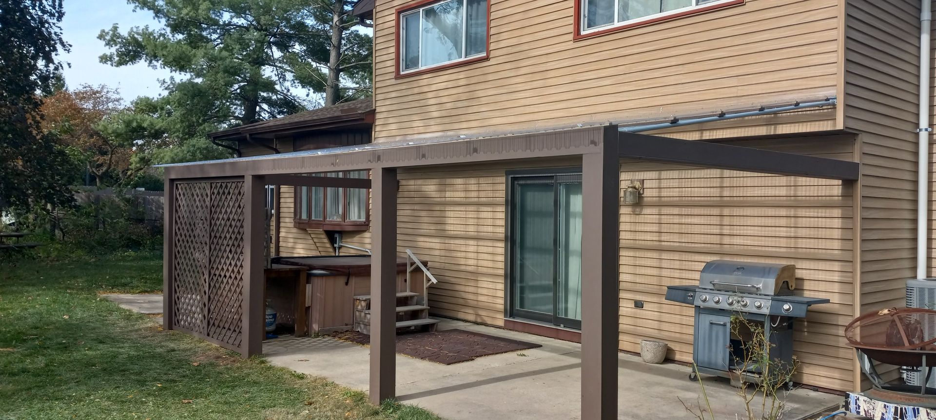 A brick house with a pergola and a grill in the backyard.