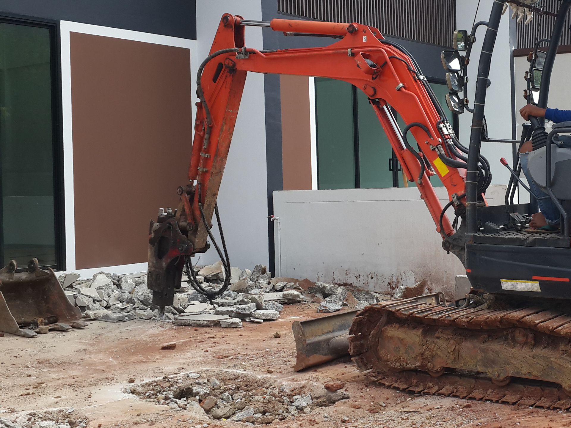 A small excavator is breaking concrete in front of a building.