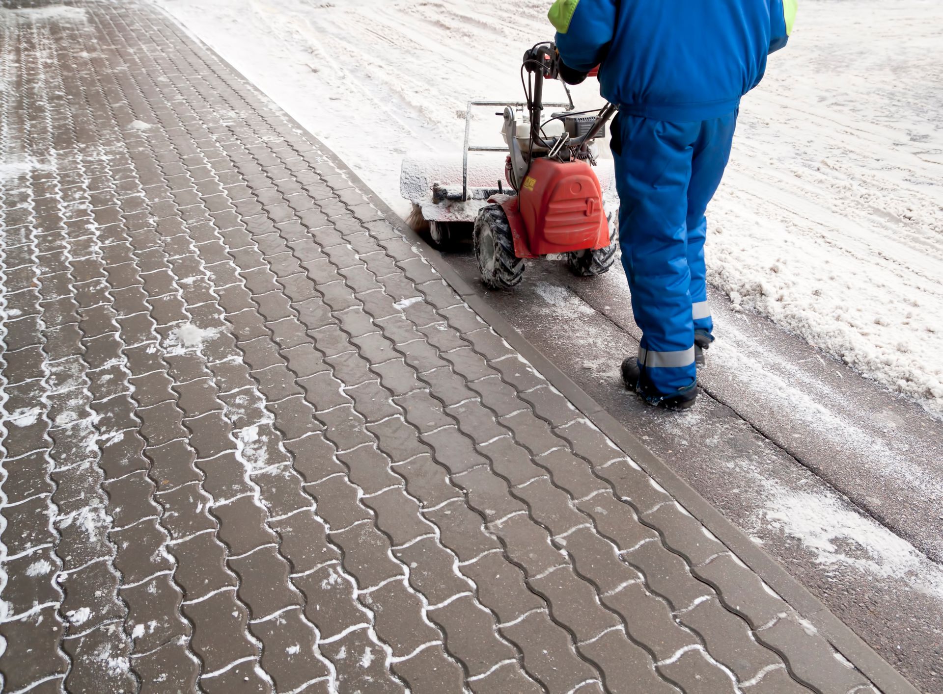 A man is cleaning the sidewalk with a snow blower.