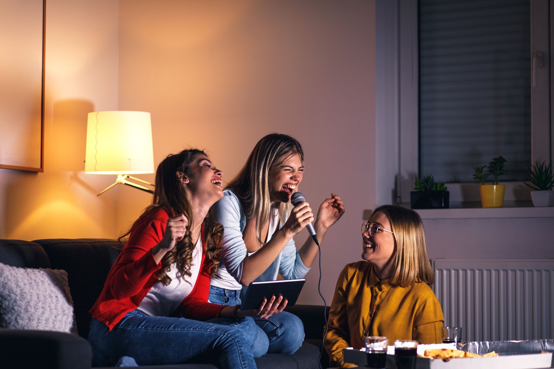 Three women are sitting on a couch singing into microphones.