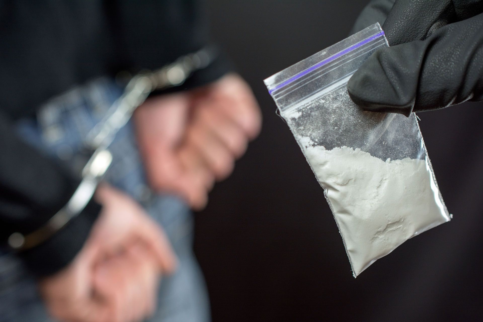 A man in handcuffs and a bag of drugs