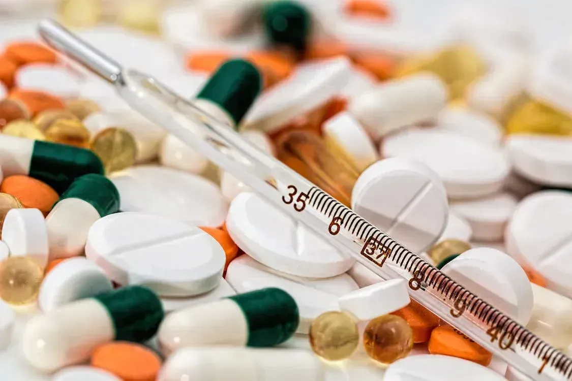 A thermometer is sitting on top of a pile of pills and capsules.