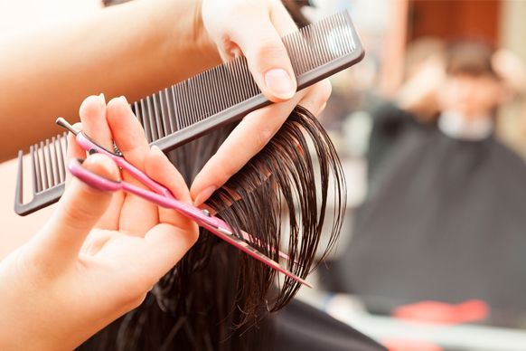Manos de un peluquero usando un peine y tijeras rosas para cortar el cabello de una clienta en un salón.