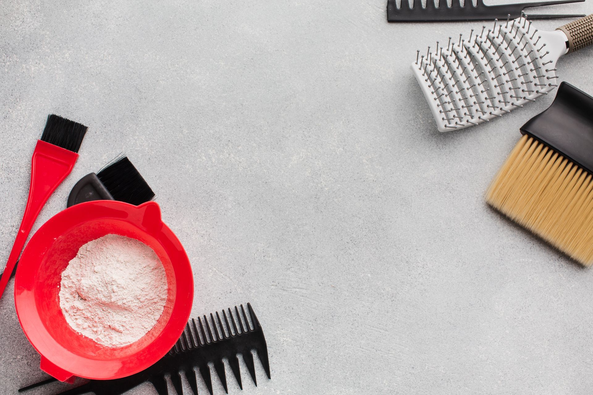 Herramientas para teñir el cabello, incluido un recipiente con polvo, cepillos y peines, dispuestos sobre una superficie gris.